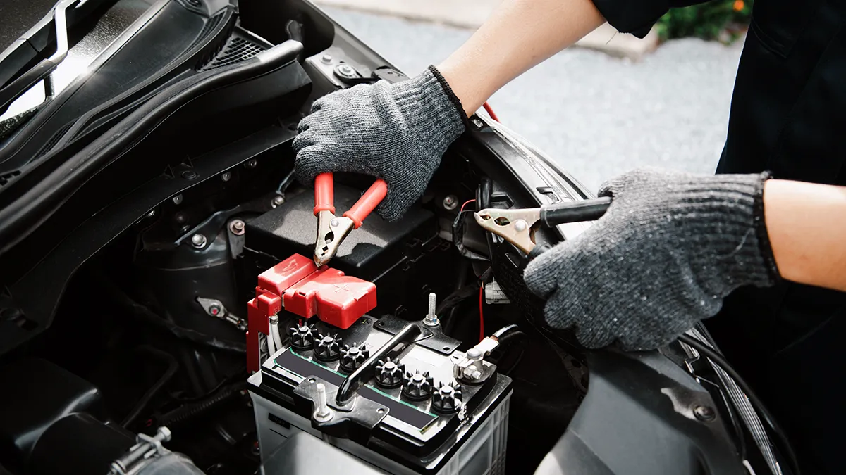 Un mécanicien en gants de travail utilise des pinces pour connecter une batterie d'auto sous le capot d'un véhicule.