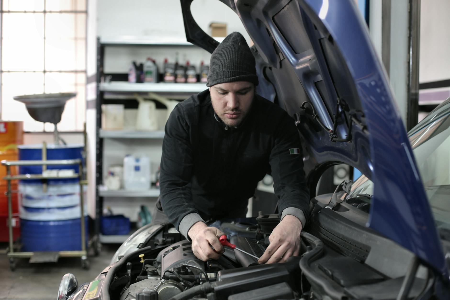 Un mécanicien en train de travailler sous le capot d'une voiture, utilisant une clé à molette dans un garage bien éclairé.