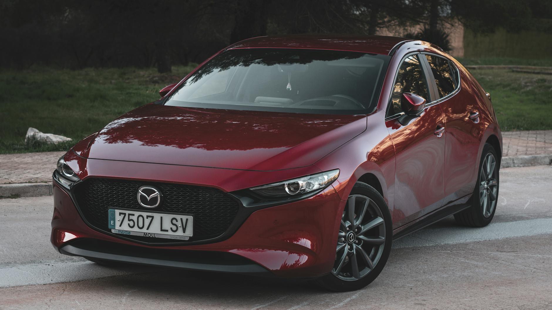 Véhicule Mazda rouge stationné sur une surface en béton, avec un arrière-plan de verdure et des rochers.