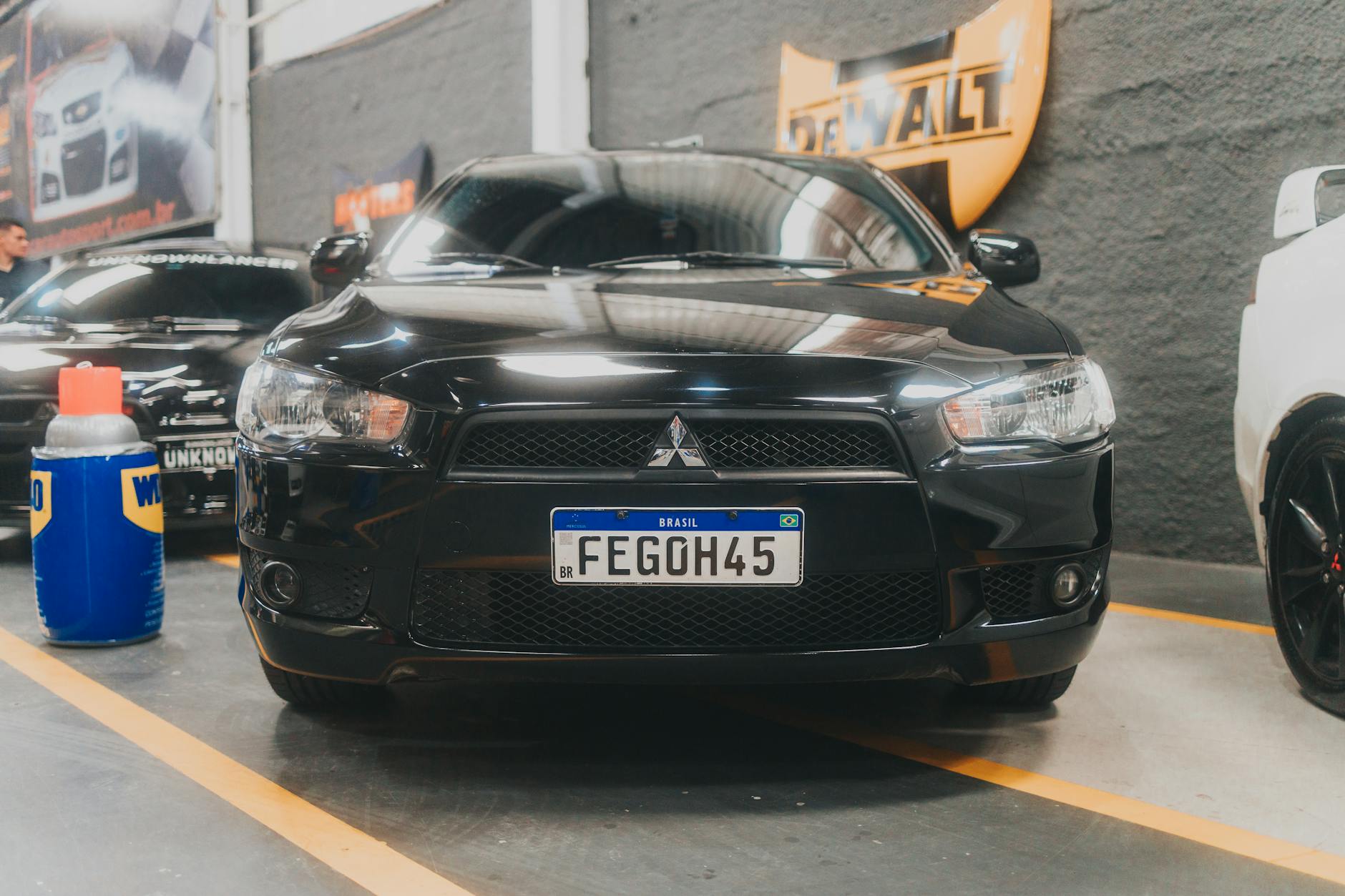 Véhicule Mitsubishi noir stationné dans un garage, avec des outils et d'autres voitures en arrière-plan.