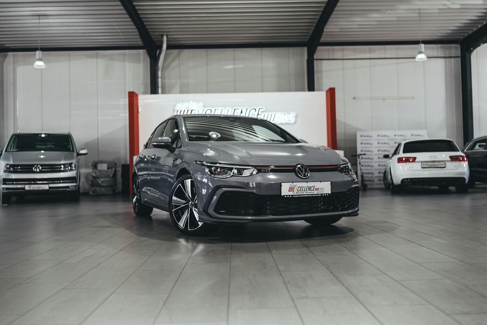 Véhicule Volkswagen gris stationné dans un garage moderne, avec d'autres voitures visibles en arrière-plan sur un sol en carrelage.