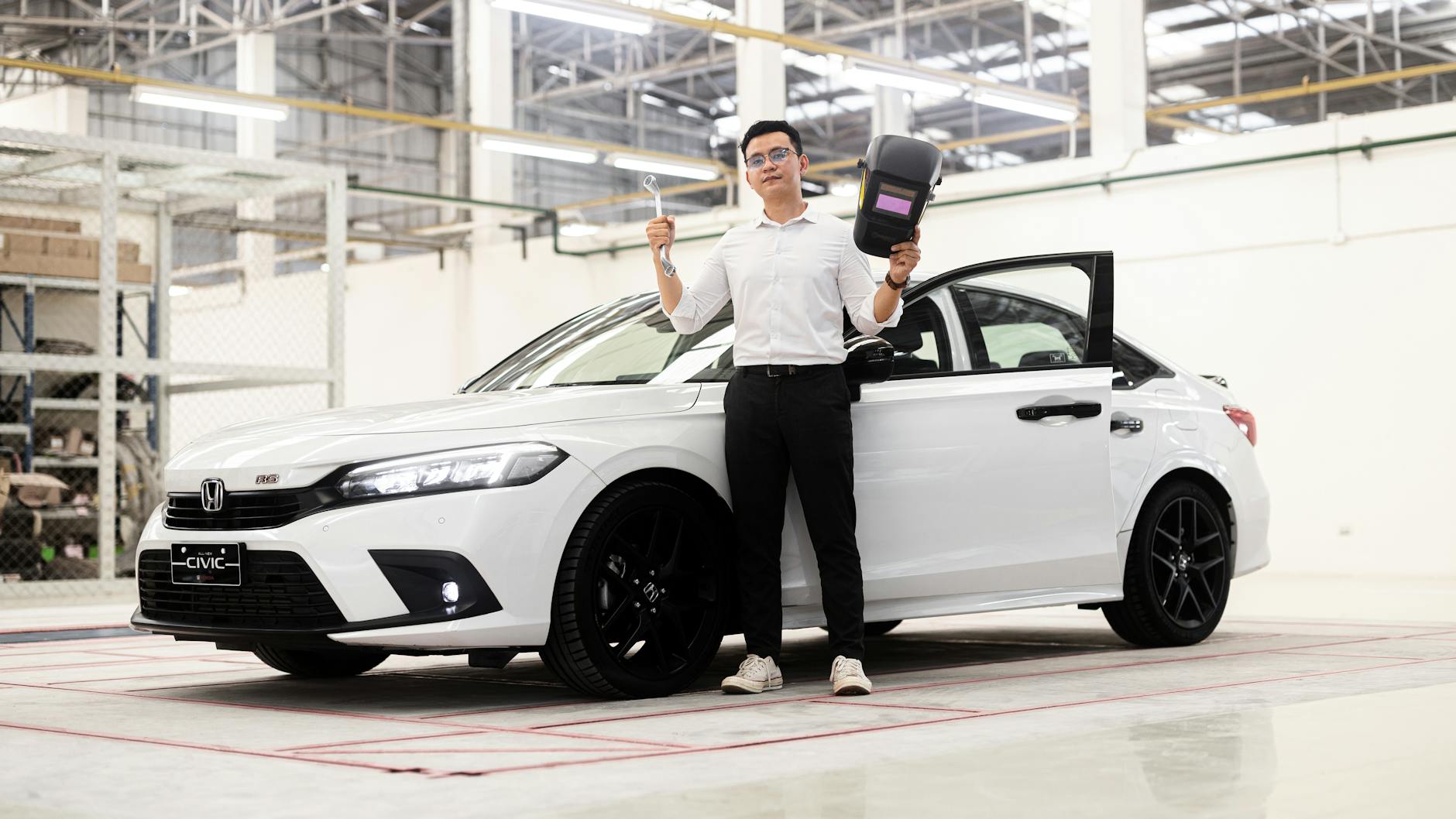 Un homme en chemise blanche se tient à côté d'une voiture Honda Civic blanche, tenant un outil dans une main et un appareil dans l'autre.