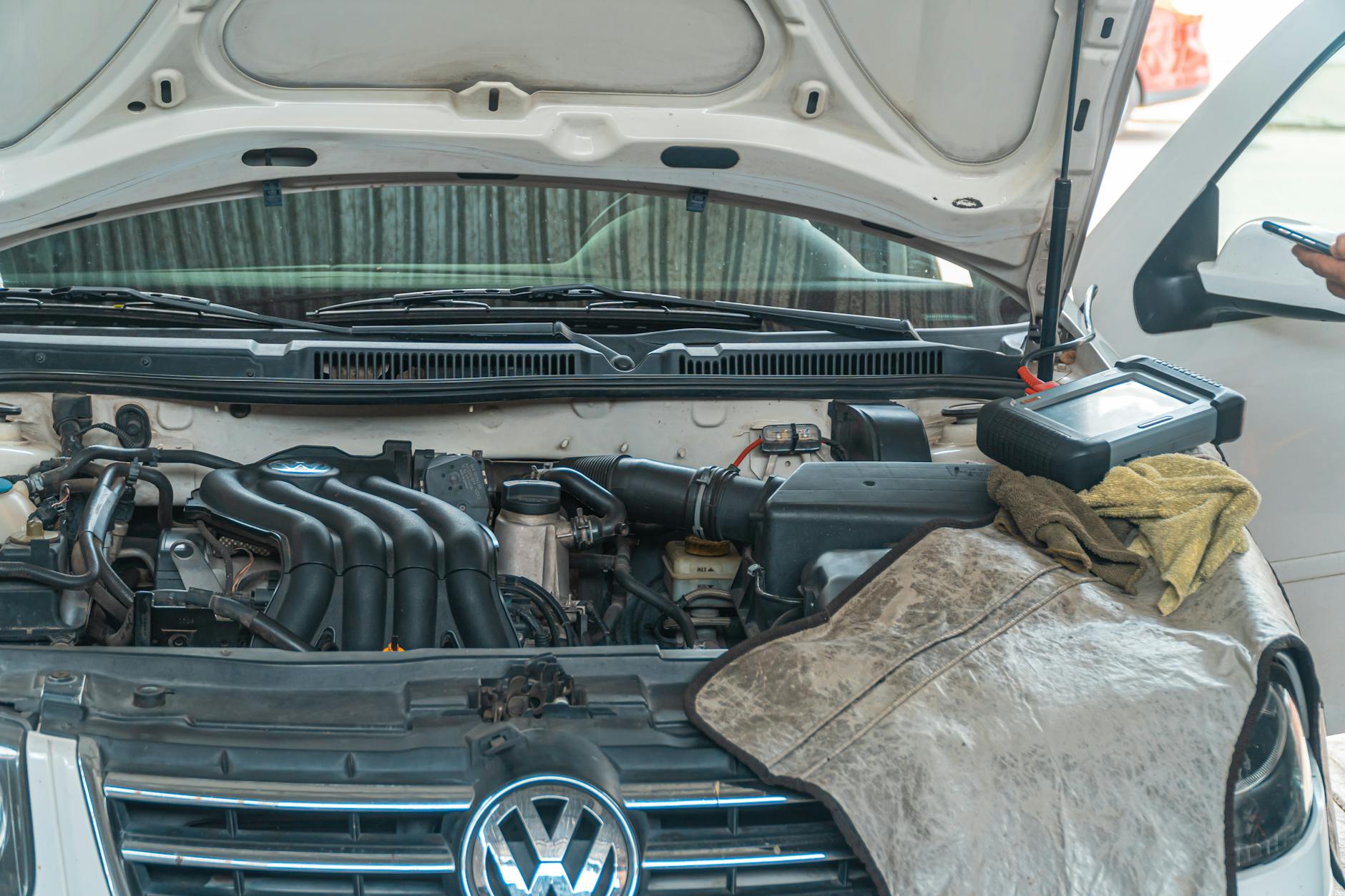 Moteur d'une voiture Volkswagen avec capot ouvert, outils et serviette sur le moteur, montrant un entretien en cours.