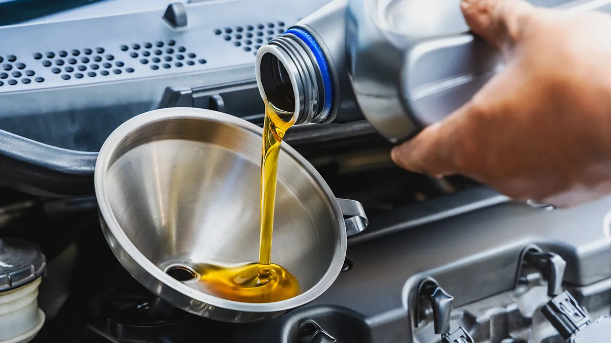 Un liquide doré est versé dans un entonnoir en métal, placé au-dessus d'un moteur de voiture.