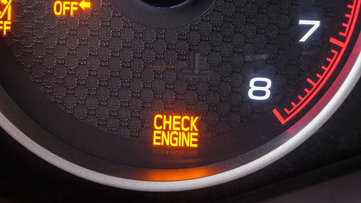 Voyant moteur allumé avec inscription "CHECK ENGINE" sur un tableau de bord, entouré d'indicateurs de vitesse et de régime moteur.