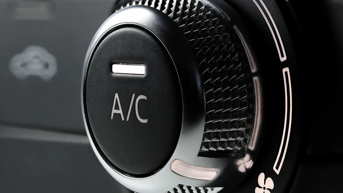 Bouton de commande du système de climatisation A/C d'une voiture, avec inscription claire et design texturé.