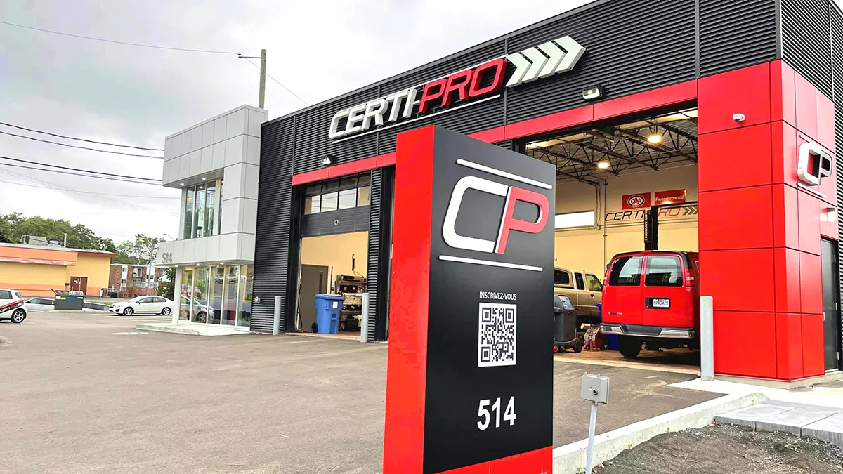Bâtiment de garage avec enseigne CertiPro, véhicules stationnés à l'extérieur et panneau d'affichage avec code QR et numéro de téléphone.