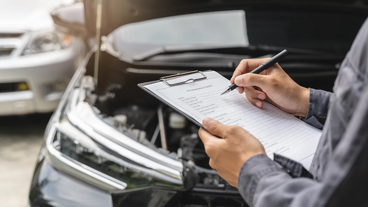 Une personne tient un clipboard avec une liste de vérification, en prenant des notes près d'un moteur de voiture ouvert.