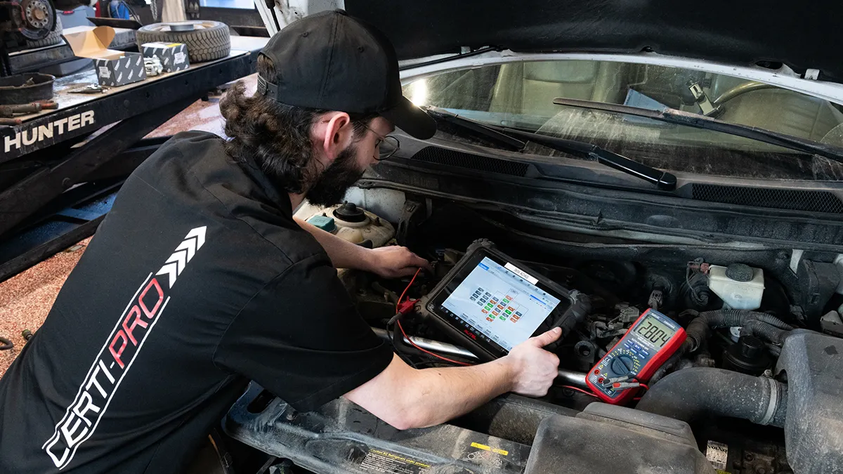 Un technicien examine le moteur d'un véhicule à l'aide d'un appareil de diagnostic et d'un multimètre, dans un garage.