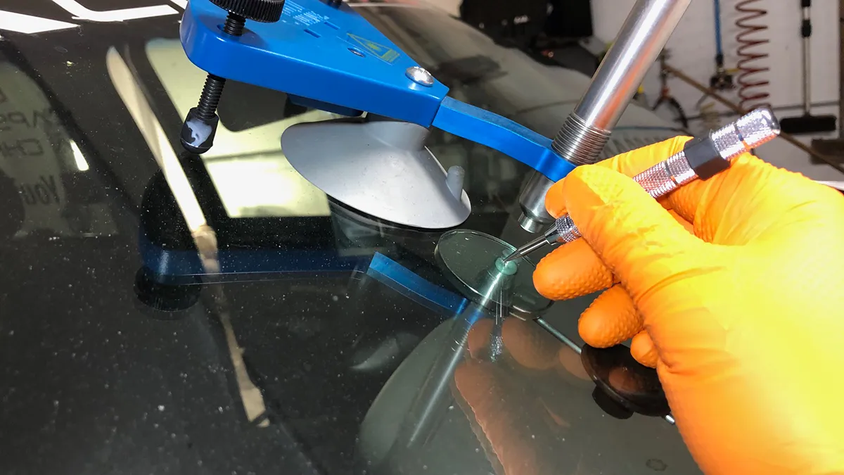 Un outil de réparation de pare-brise est utilisé, avec une main gantée tenant un injecteur sur une surface de verre.