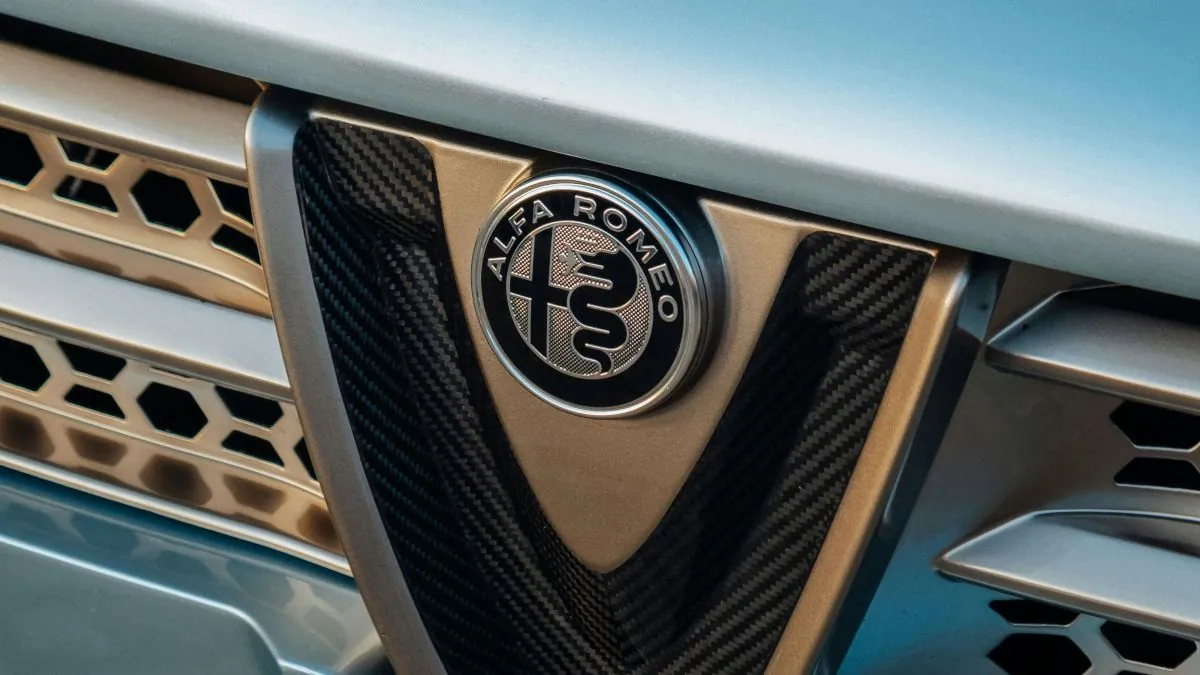 Logo d'Alfa Romeo sur la calandre d'une voiture, avec un design en métal et des éléments en carbone, mettant en avant l'identité de la marque.