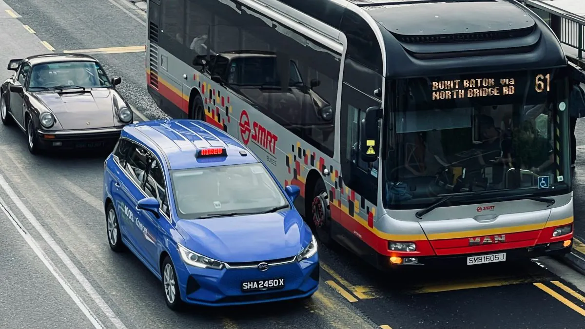 Un autobus de transport en commun croise une voiture bleue et une voiture de sport sur une route urbaine.