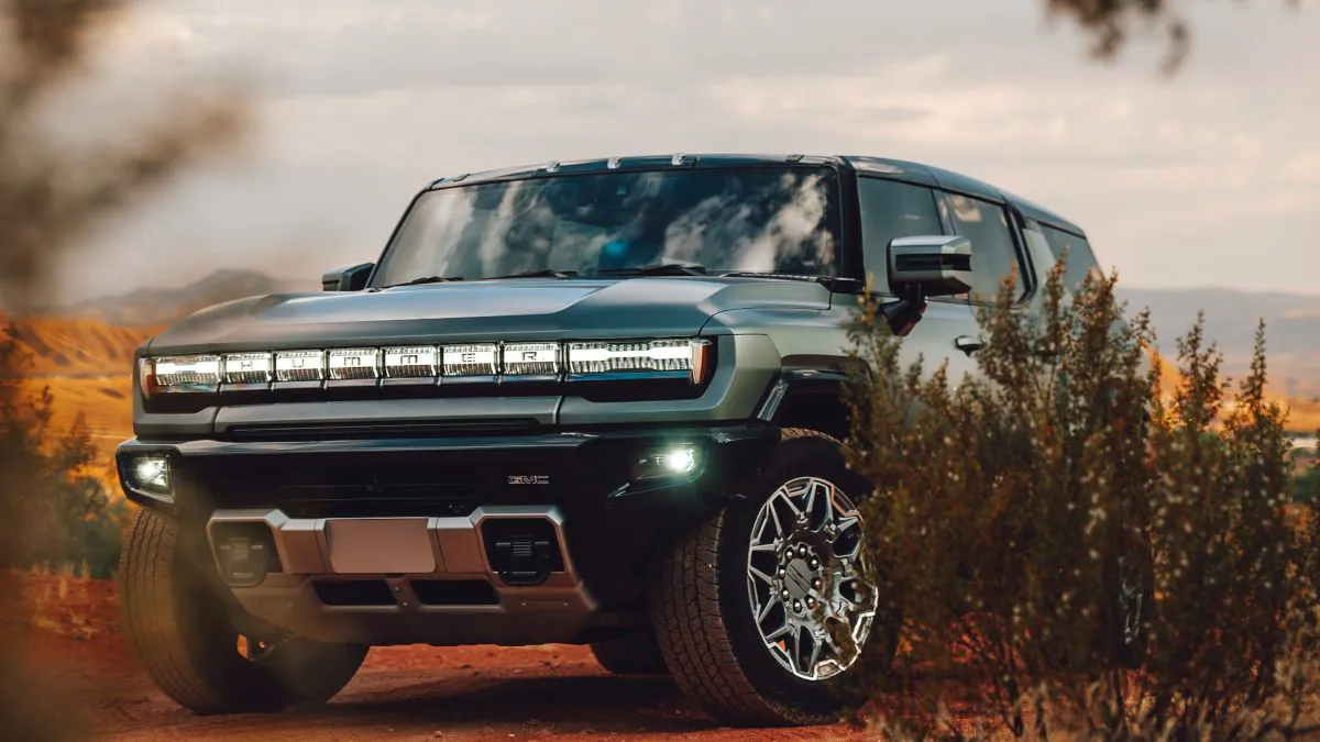 Véhicule Hummer noir avec des phares LED, garé sur un terrain désertique, entouré de végétation et sous un ciel nuageux.