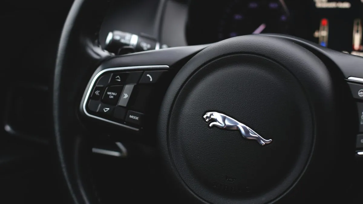 Volant de voiture avec logo Jaguar, boutons de contrôle sur le côté, tableau de bord flou en arrière-plan.