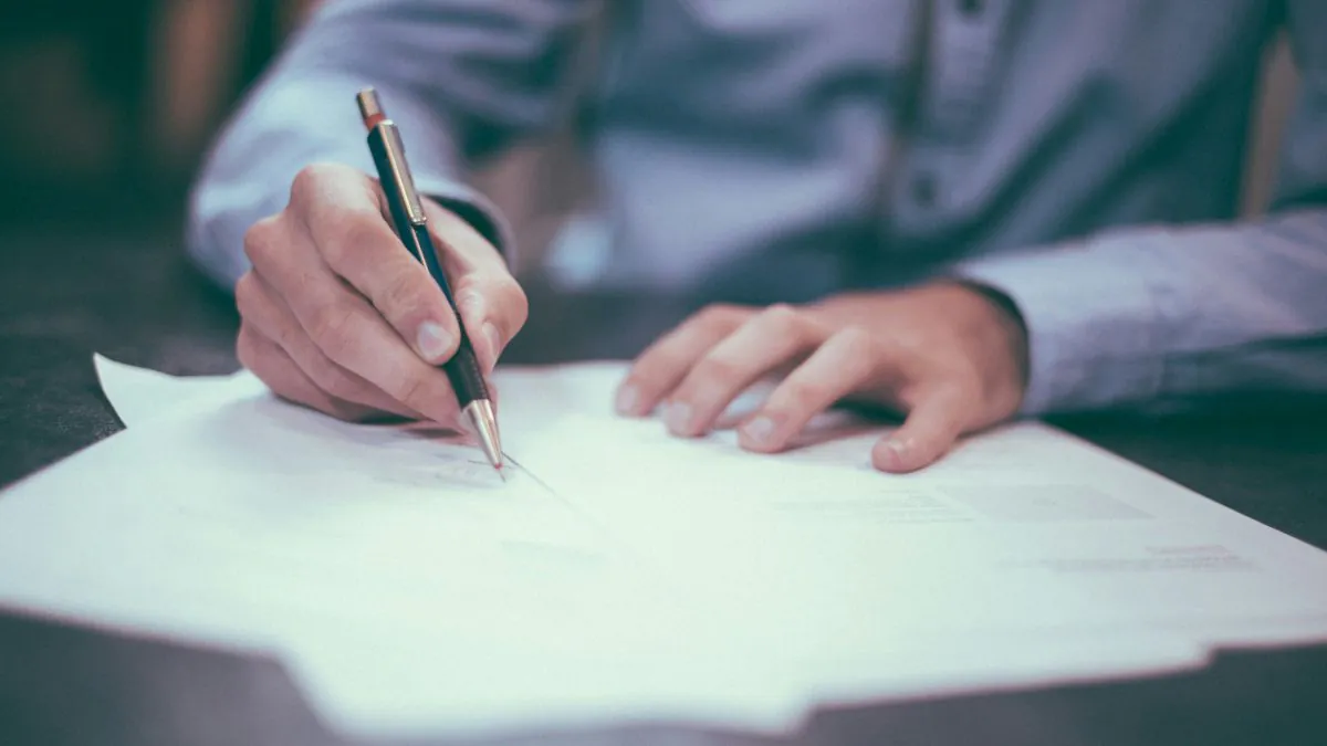Une main tenant un stylo signe des documents posés sur une surface, suggérant un processus de décision ou d'engagement.