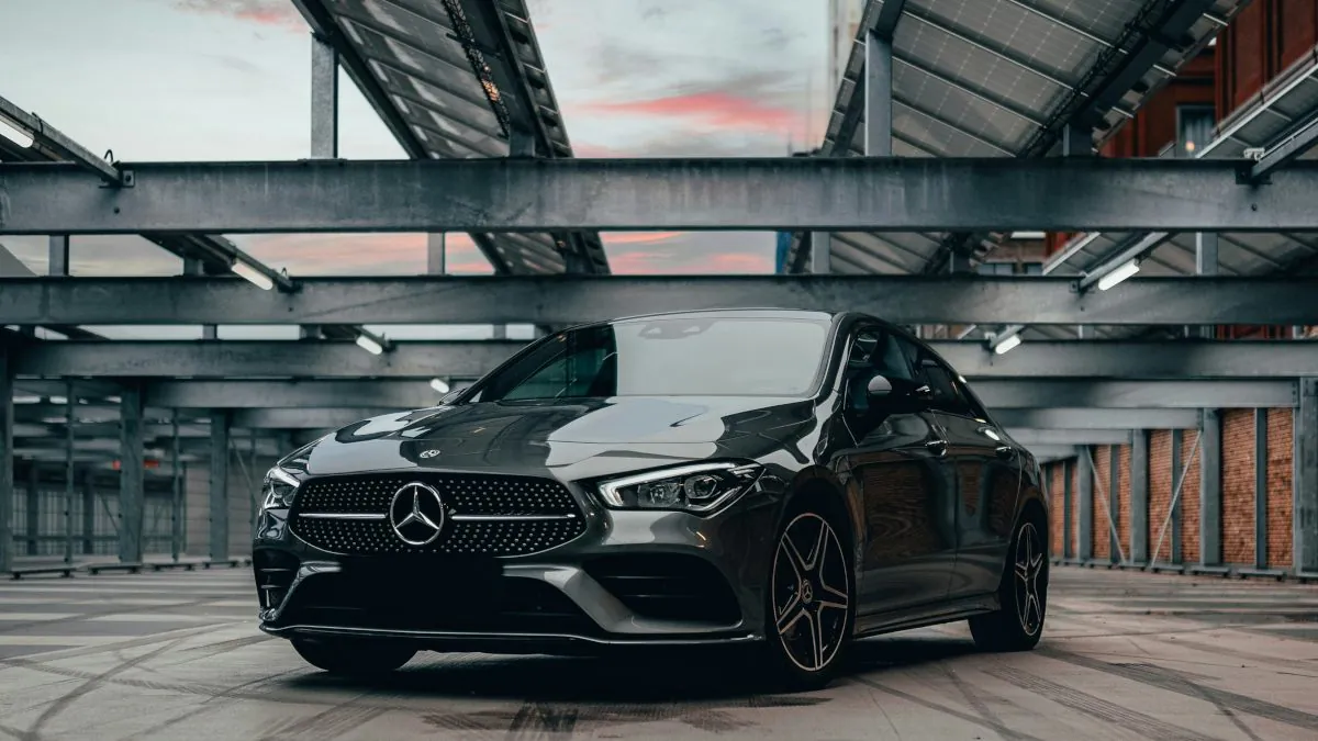Véhicule Mercedes de couleur grise stationné dans un garage moderne, avec des structures métalliques et un ciel nuageux en arrière-plan.