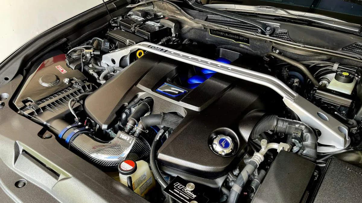 Moteur automobile avec des composants visibles, incluant des tuyaux, un réservoir et un couvercle en plastique, dans un compartiment bien éclairé.