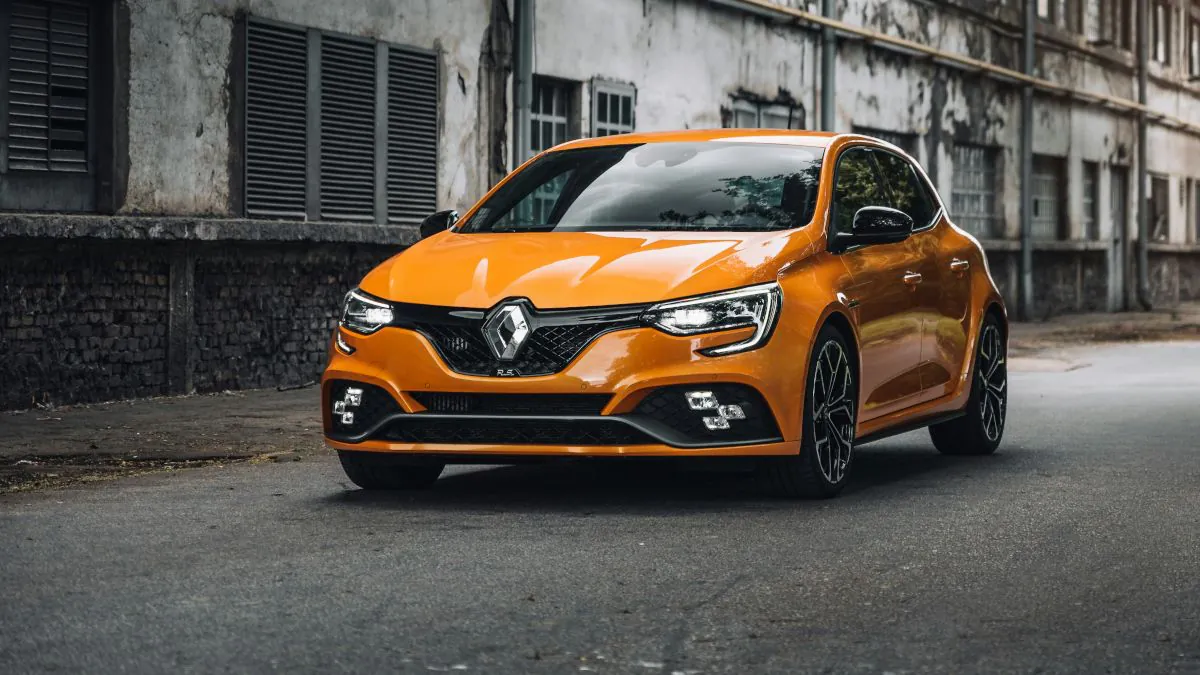 Voiture Renault de couleur orange stationnée sur une route, avec un bâtiment en arrière-plan.