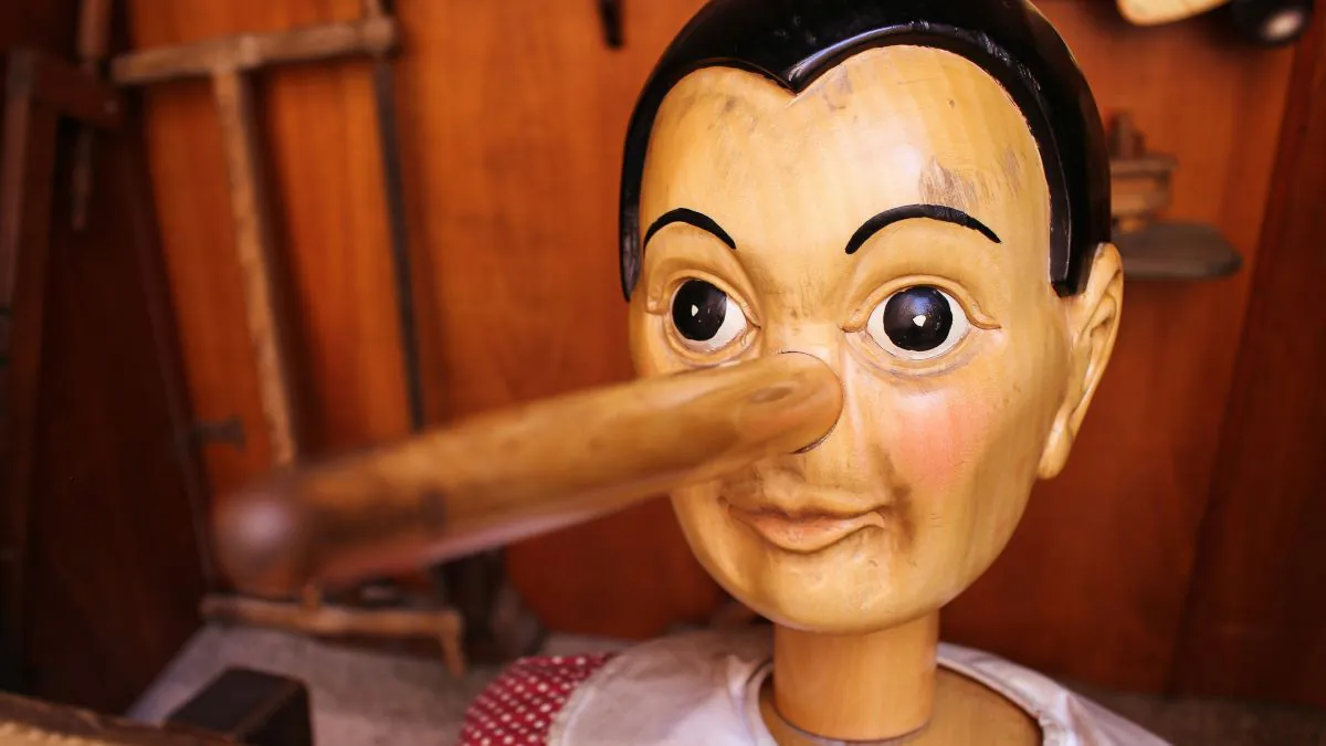 Poupée en bois avec un nez allongé, représentant un personnage mythique associé au mensonge, sur fond de bois.